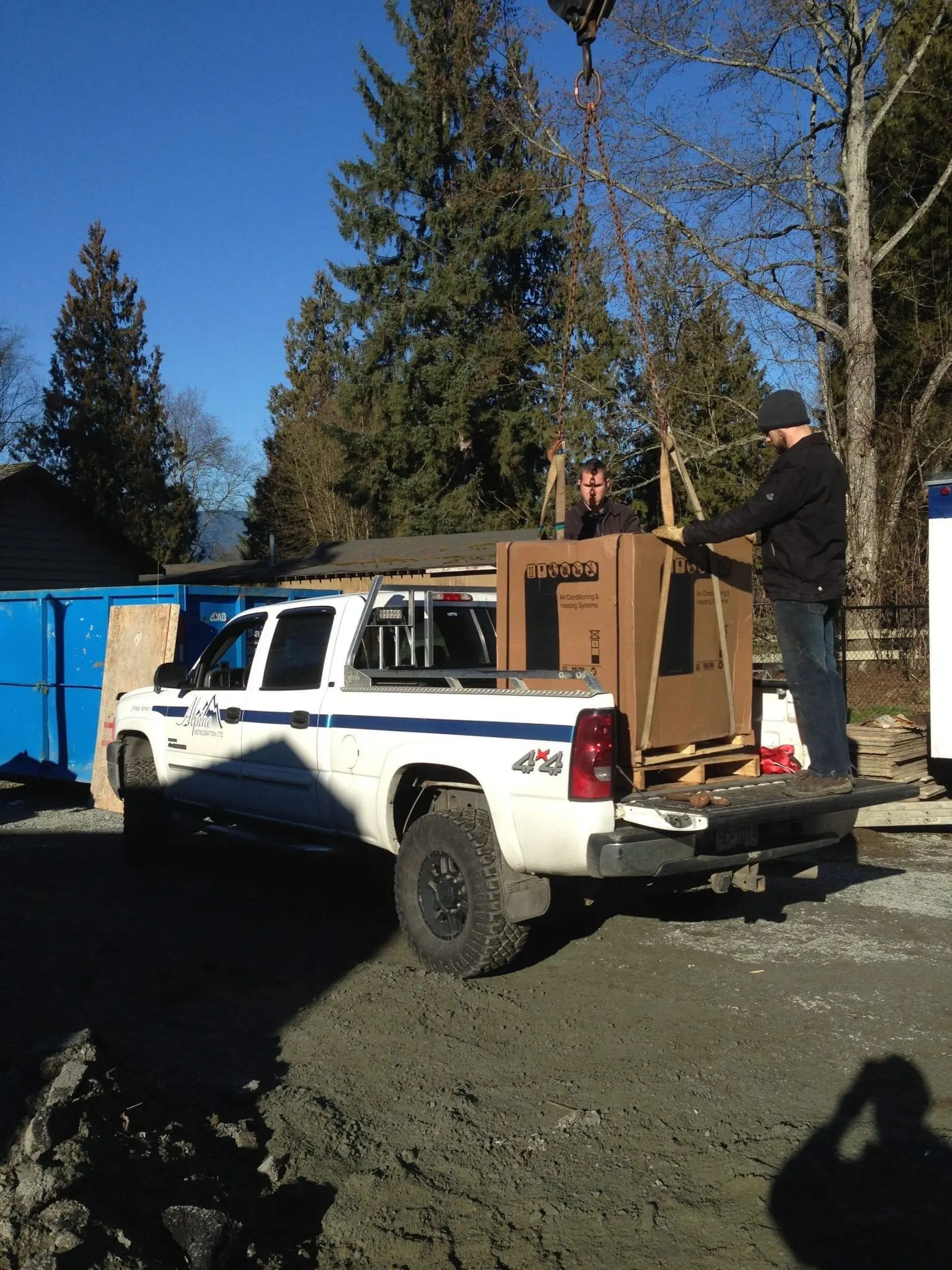Alpine Refrigeration technicians using crane to lift HVAC equipment onto truck
