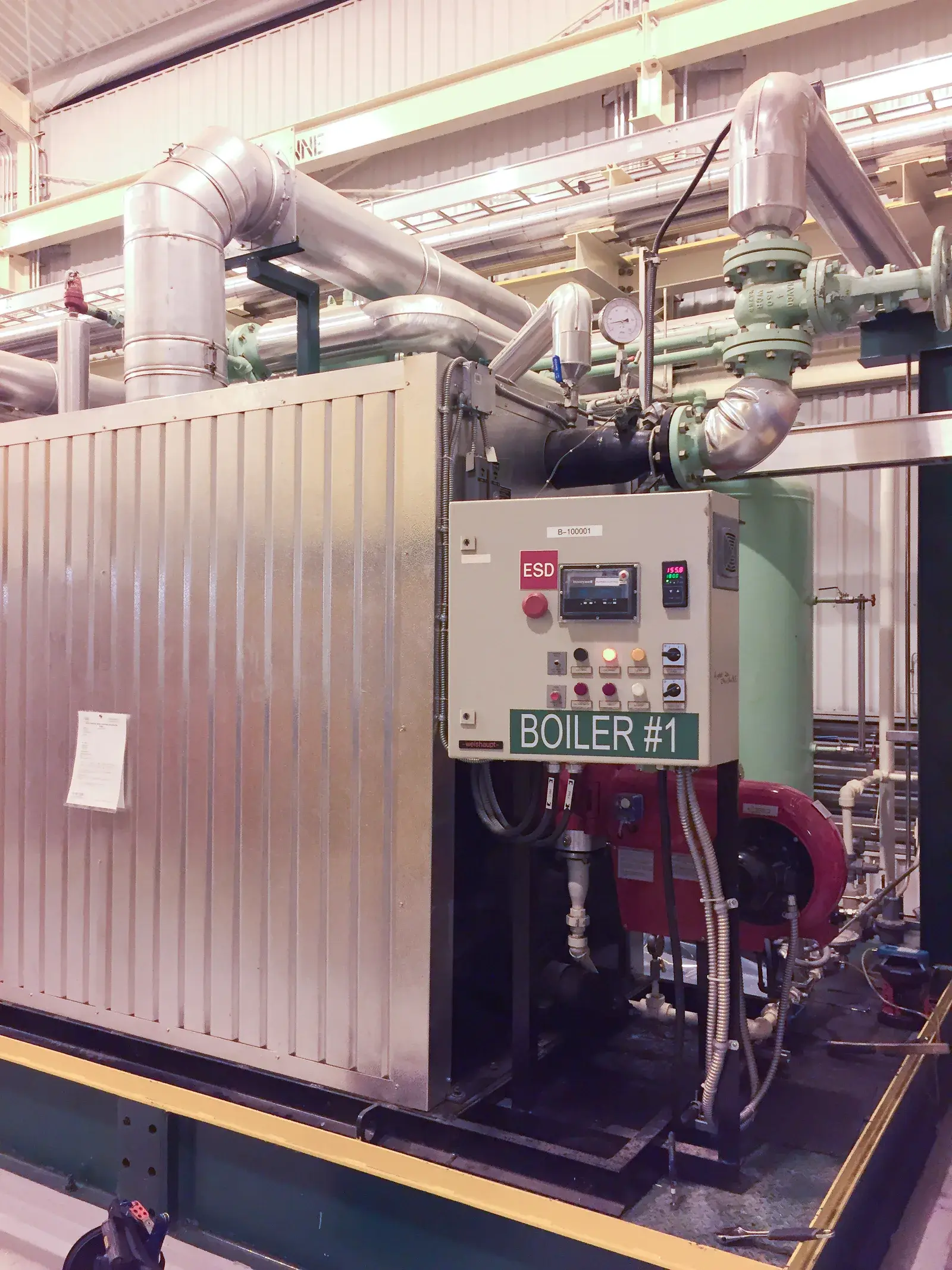 Weishaupt-fired commercial boiler with ESD control panel, insulated steam piping, and isolation valves in an industrial mechanical plant