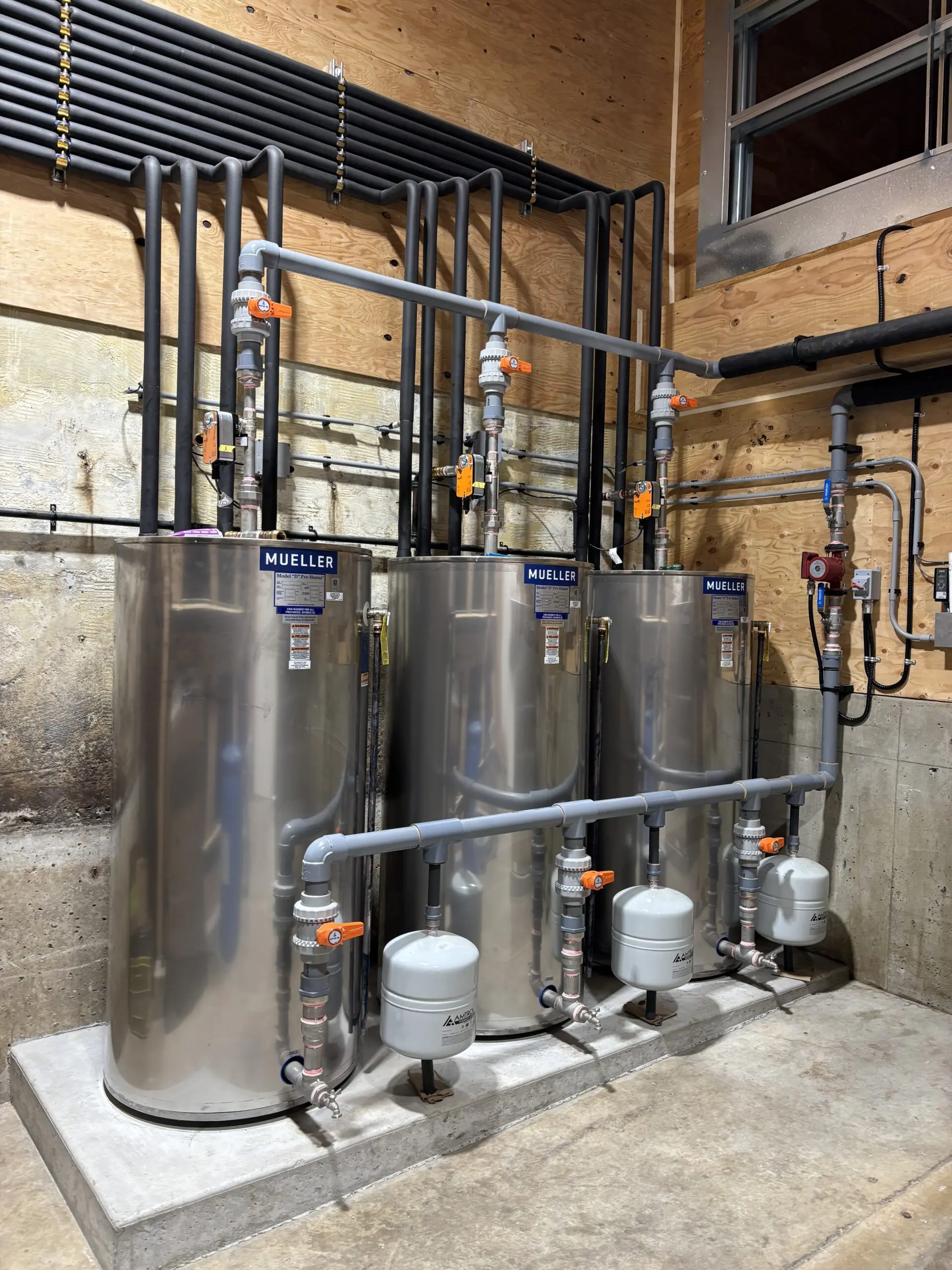 Three stainless steel tanks with pipes in a dairy refrigeration system.